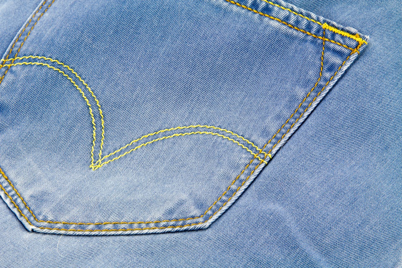 Detailed close-up of blue denim jeans pocket with yellow stitching, highlighting the texture and design.